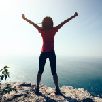 freedom female standing  with outstretched arms on sunrise windy coast