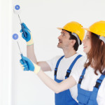 Team of young workers in hardhats painting the wall