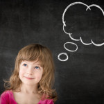 Smart kid in class. Happy child against blackboard. Drawing speech bubble cloud